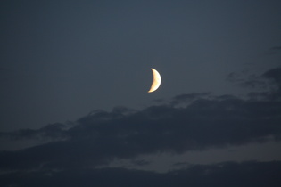 der zunehmende Mond in einer Wolkenlücke